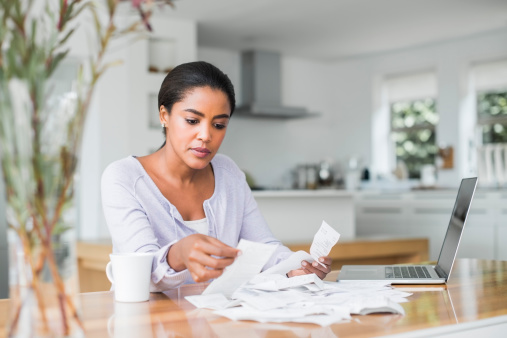 Mid adult woman reading bills while making online payment at home